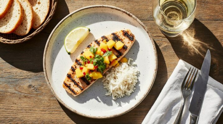 Gegrilltes Fischfilet mit frischer Mango-Salsa, serviert mit Jasminreis und Limette auf einem weißen Teller, daneben ein Glas Whitehaven Sauvignon Blanc aus Neuseeland