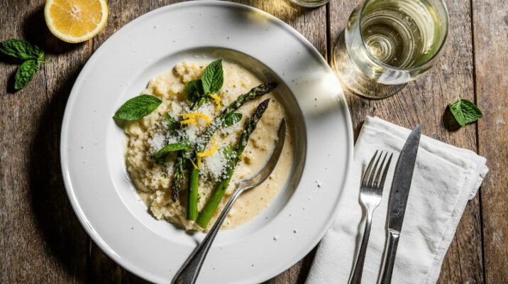Cremiges Zitronen-Risotto mit grünem Spargel, frischer Minze und Parmesan in einer weißen Schale, daneben ein Glas Weißwein aus Neuseeland