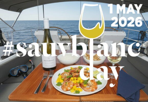Gegrillte Garnelen mit Mango-Avocado-Salsa und Limettenbutter auf einem weißen Teller, garniert mit Koriander und Limettenringen, daneben ein elegantes schlankes Weißweinglas mit Sauvignon Blanc Whitehaven aus Marlborough, Neuseeland, leicht beschlagen.