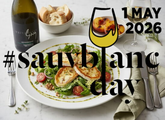 Gegrillter Ziegenkäse-Salat mit Kräutervinaigrette, Walnüssen und Kirschtomaten auf einem flachen Teller, daneben ein elegantes schlankes Weißweinglas mit Sauvignon Blanc Greg Whitehaven aus dem Awatere Valley, Marlborough, Neuseeland, leicht beschlagen.