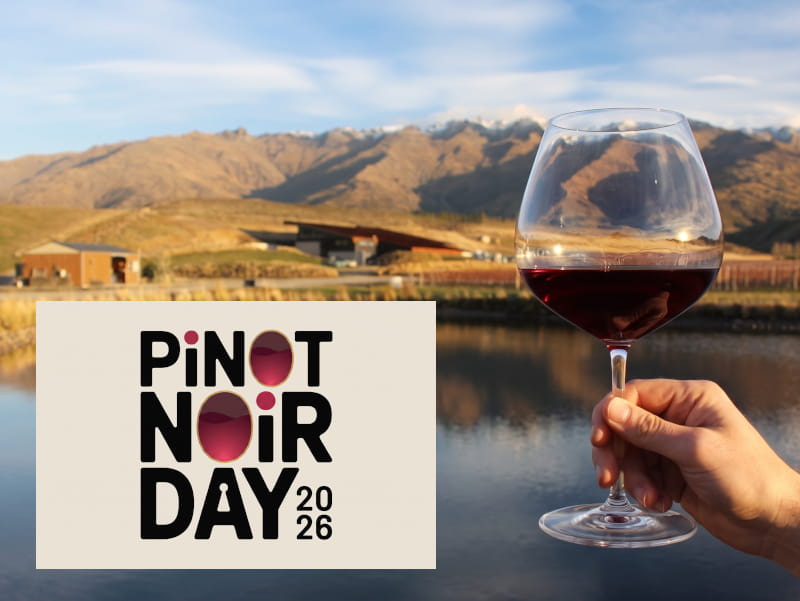 Hand hält ein großes, halb gefülltes Rotweinglas mit Pinot Noir vor der Weinberglandschaft von Amisfield in Central Otago, Neuseeland, mit Bergpanorama und See; im Vordergrund das Logo „Pinot Noir Day 2026“.